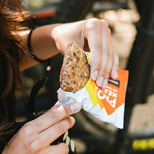 Person holding an energy bar outdoors.